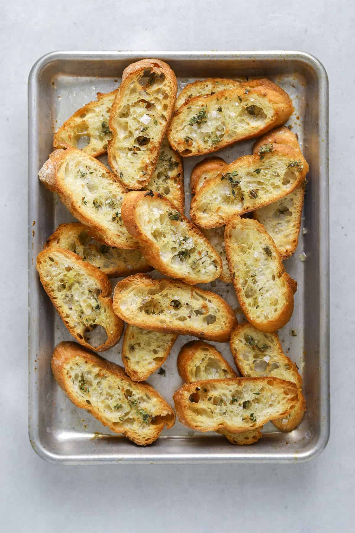 golden brown, baked crostini piled up on a baking tray on a blue background
