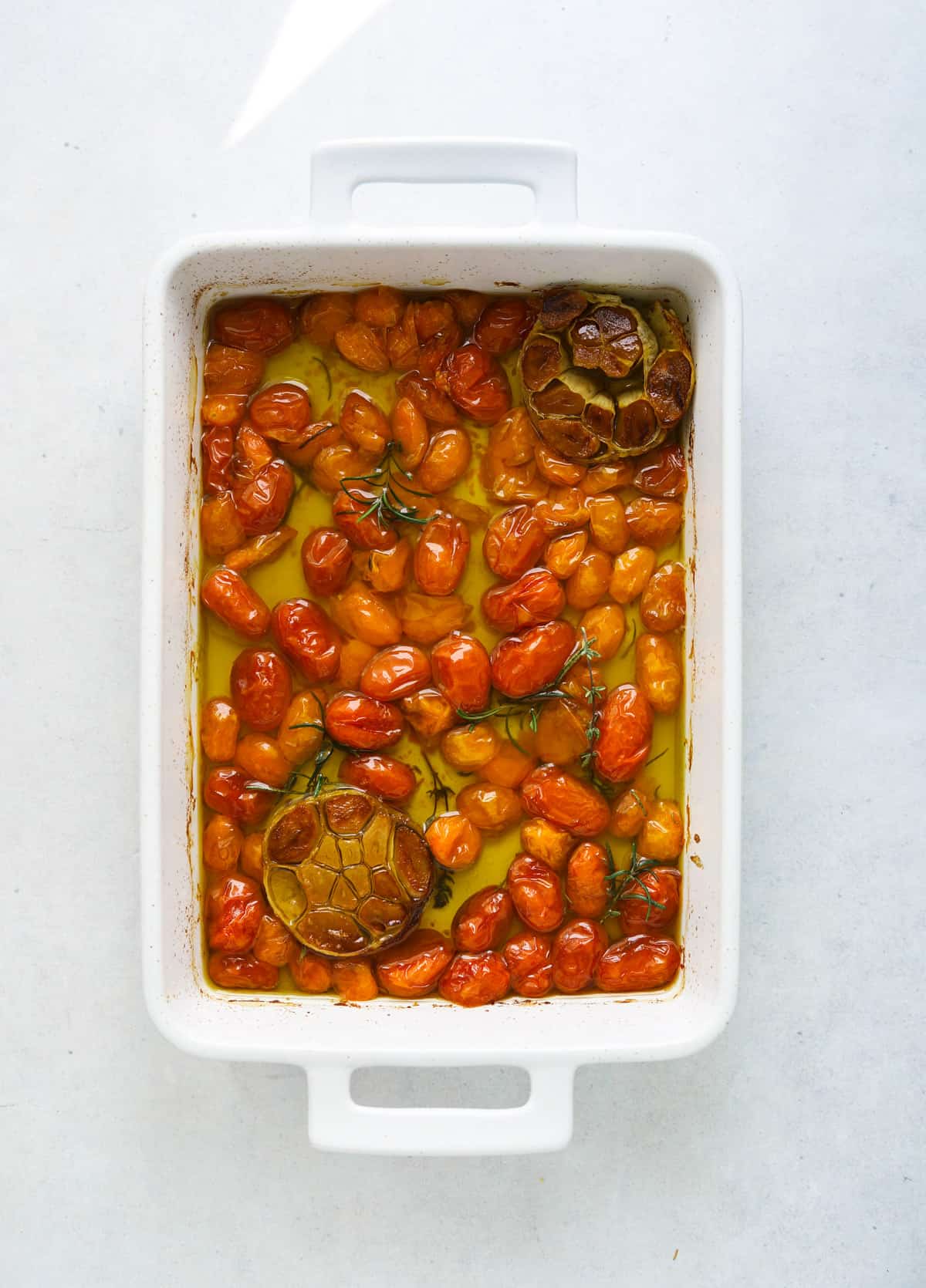 a white rectangle baking dish with roasted cherry tomatoes, olive oil and roasted garlic