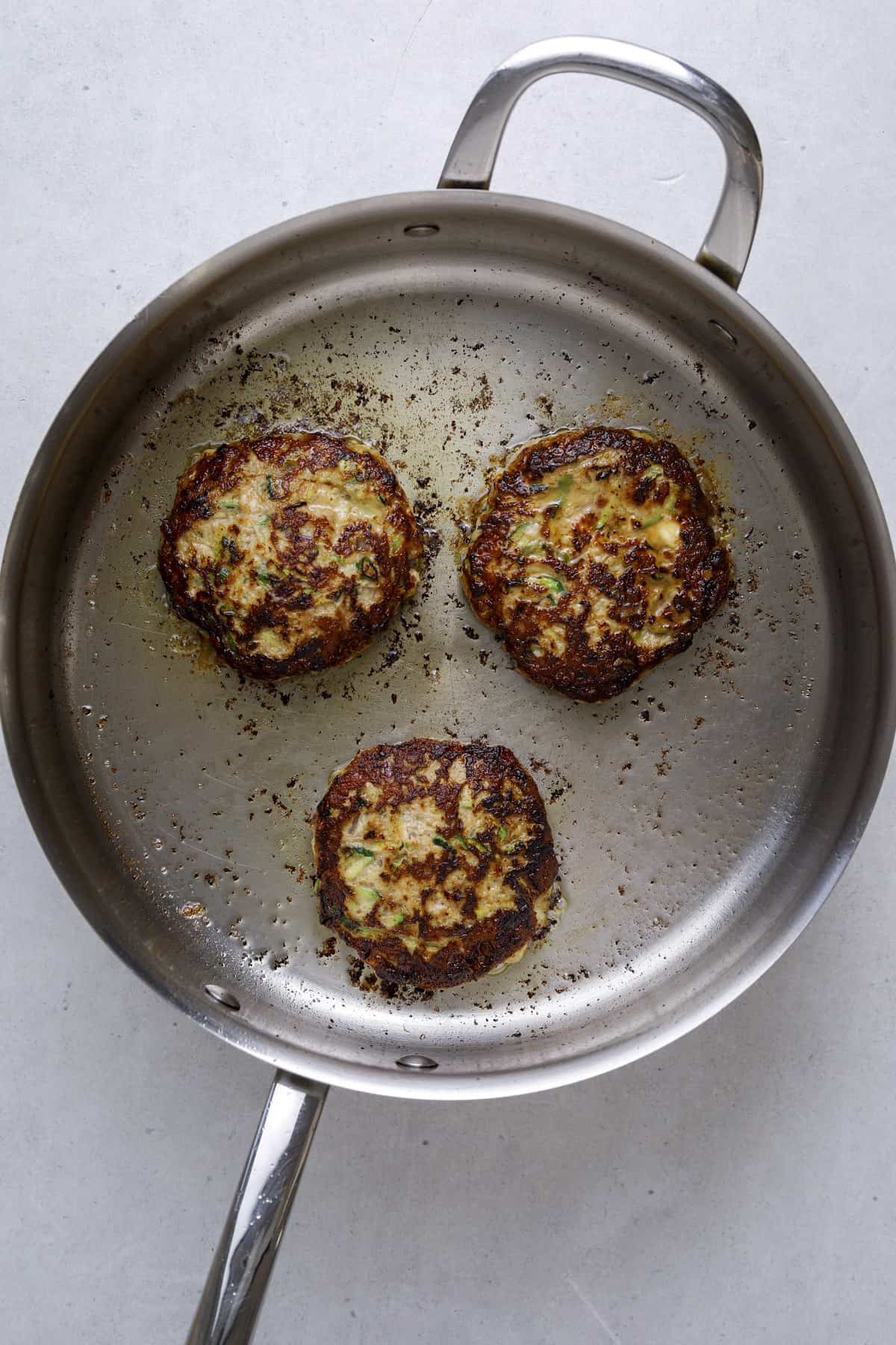 a stainless steel pan with three turkey burgers cooking