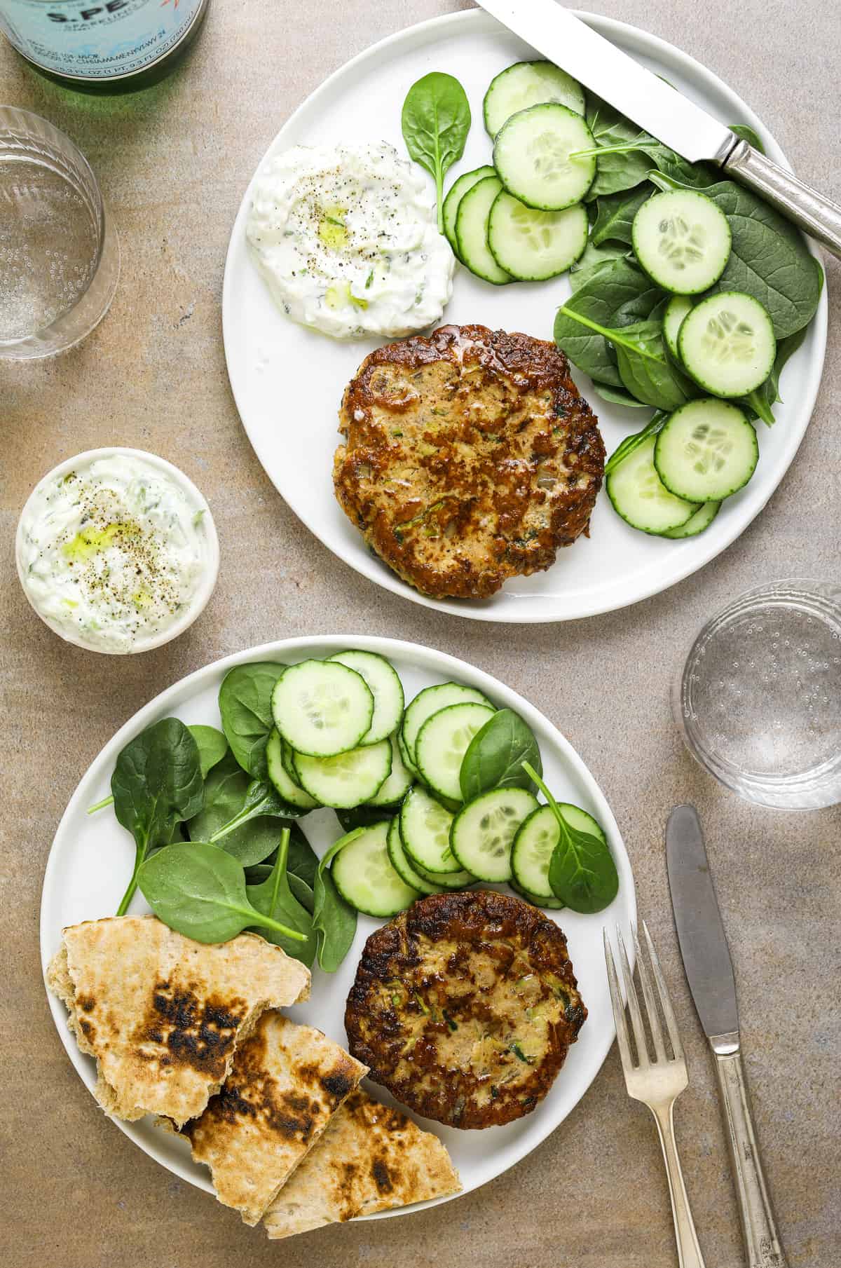 two white plates with turkey burgers and side salads with pita bread and silverware