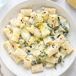 a white speckled ceramic bowl filled with creamy ricotta pasta, lemon zest and wilted spinach.