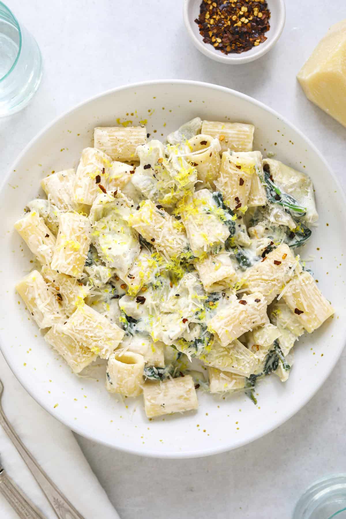 a white speckled ceramic bowl filled with creamy ricotta pasta, lemon zest and wilted spinach.