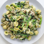 a light blue plate piled high with orecchiette pasta, crumbled sausage, broccoli rabe and topped with grated parmesan cheese