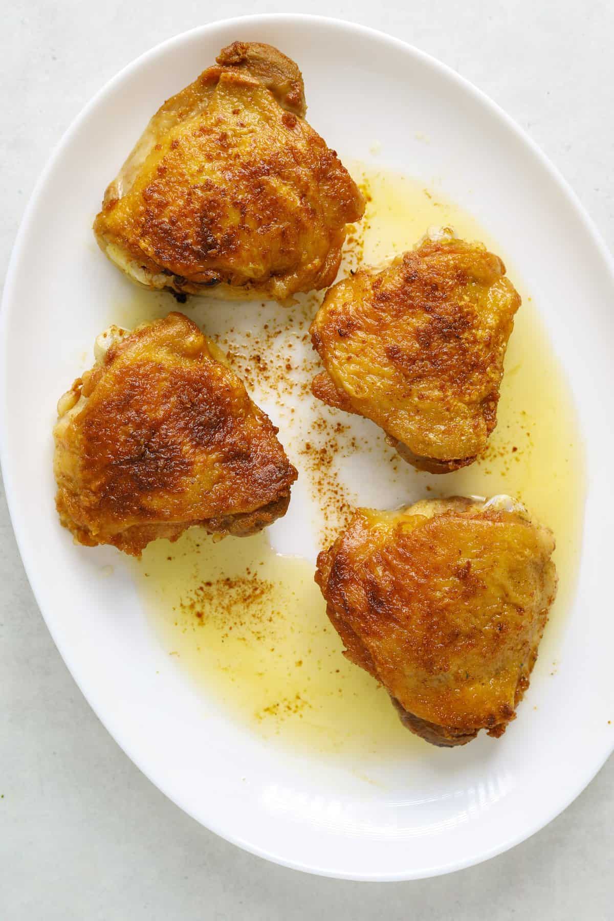 a white oval platter with four golden brown chicken thighs