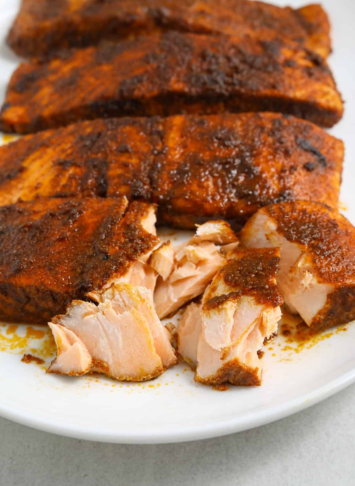 a close up image of BBQ salmon filets coated in spices on a white oval platter.