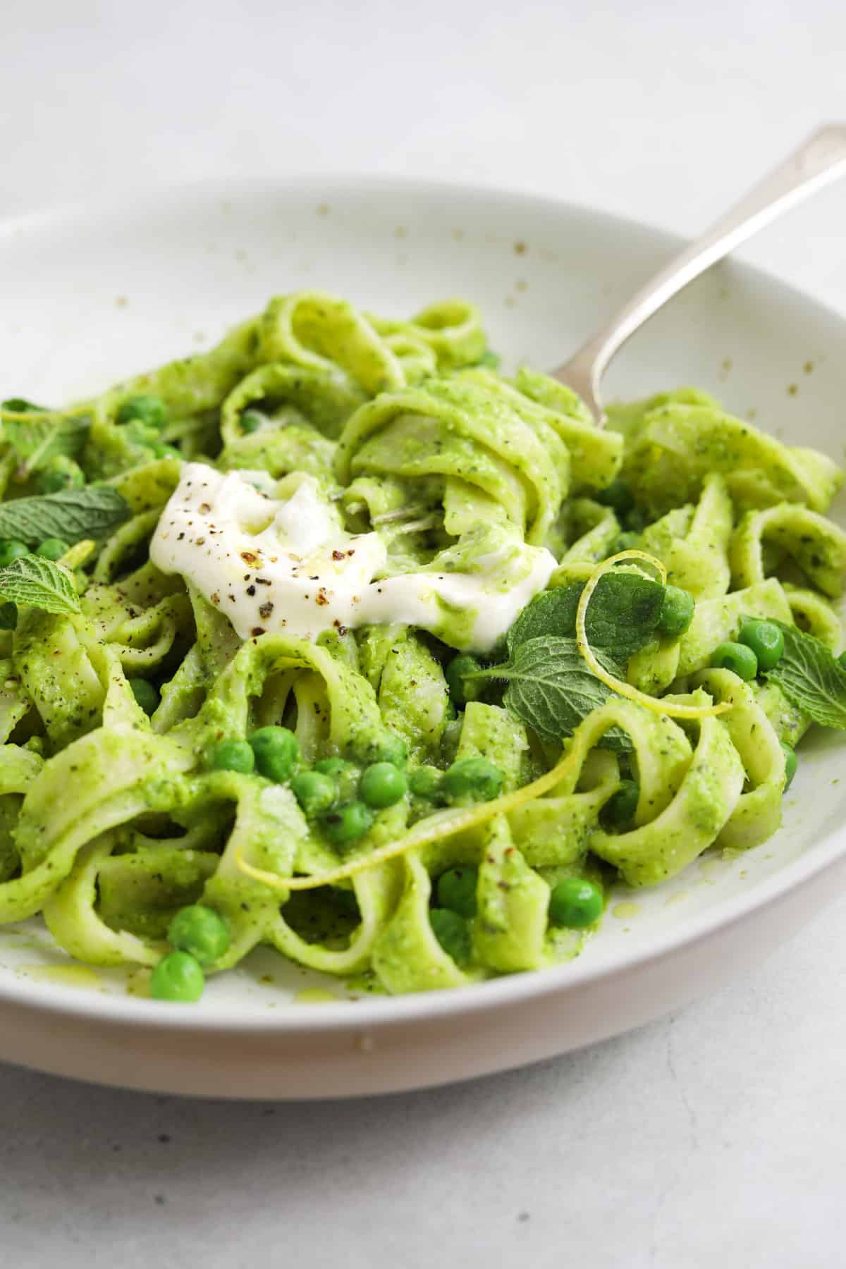 a close up, messy bowl of green pesto pasta with a fork digging into the center.