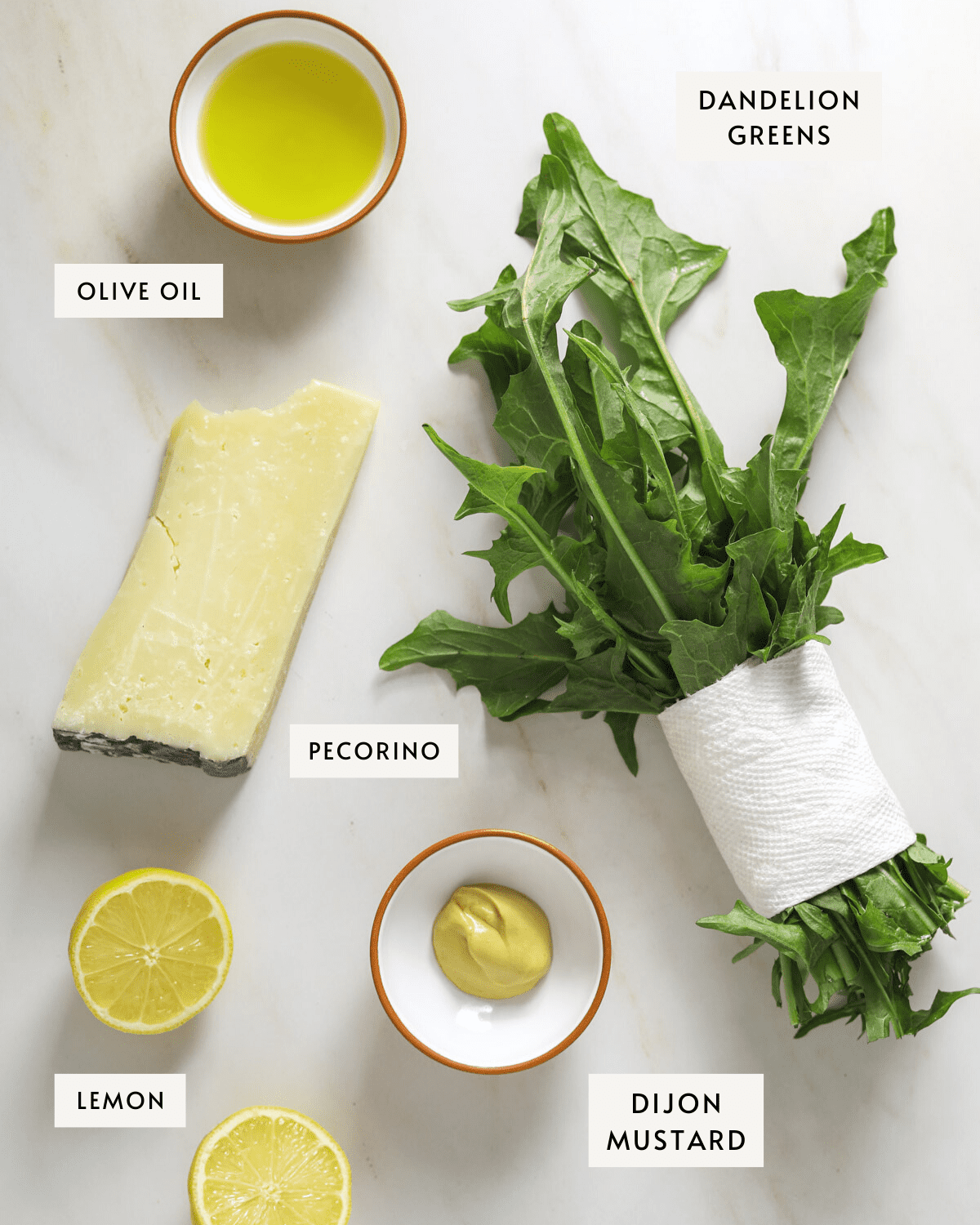 a chunk of pecorino cheese, a bowl of olive oil, a bundle of dandelion greens, a lemon sliced in half, a small dish of dijon mustard.