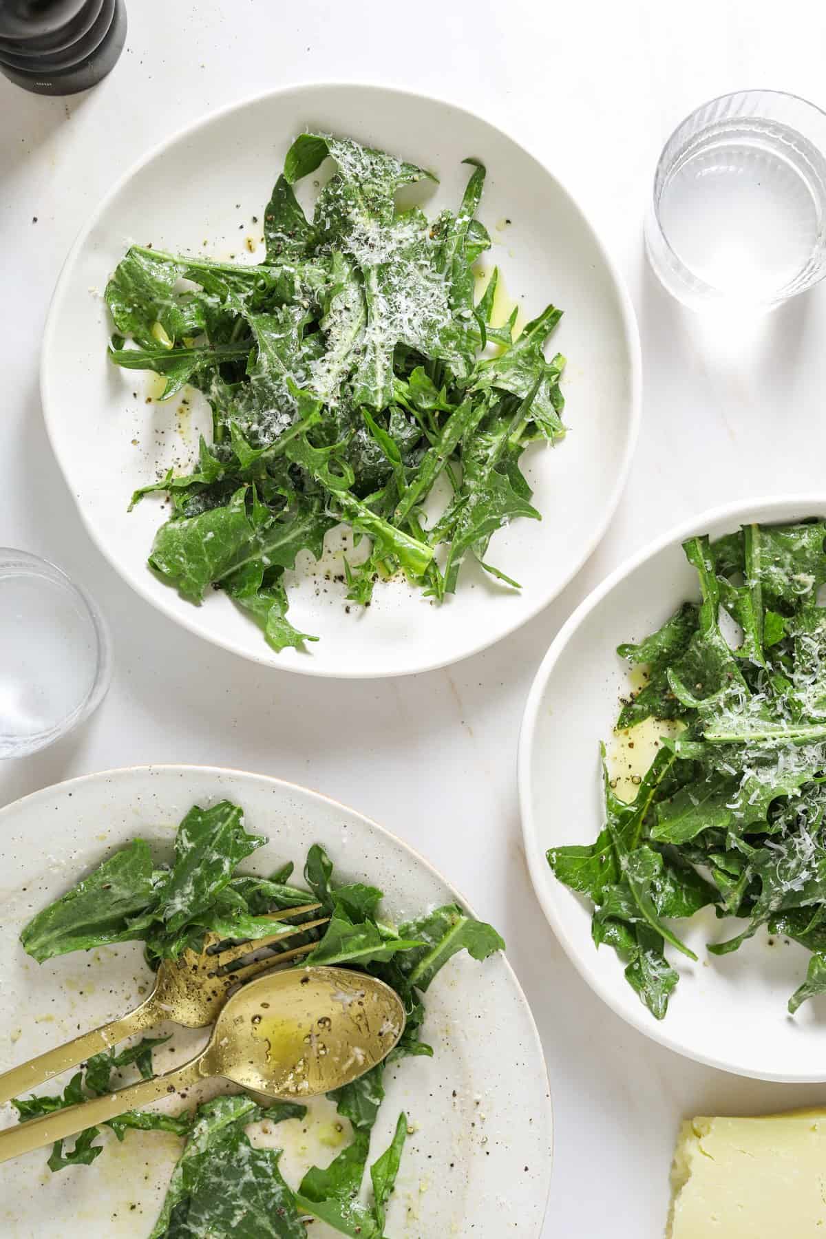 two white bowls of dandelion salad topped with shaved pecorino and cracked black pepper.