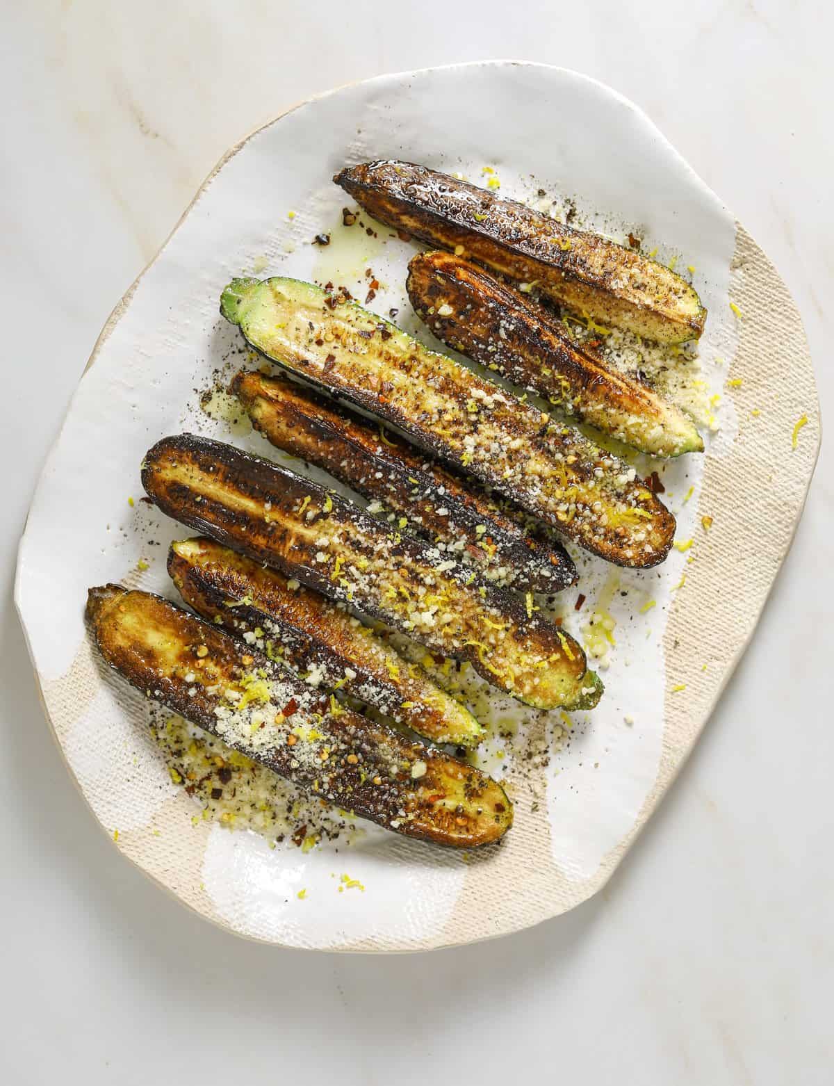 A large beige platter on a marble background filled with roasted zucchini.
