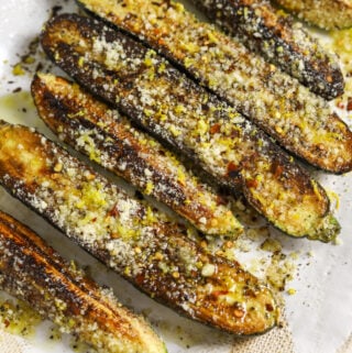 Seven pieces of zucchini on a platter, topped with grated cheese, lemon zest and chili flakes.