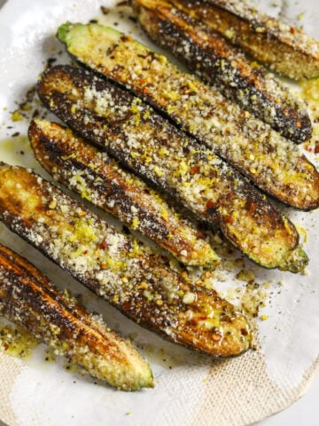 Seven pieces of zucchini on a platter, topped with grated cheese, lemon zest and chili flakes.