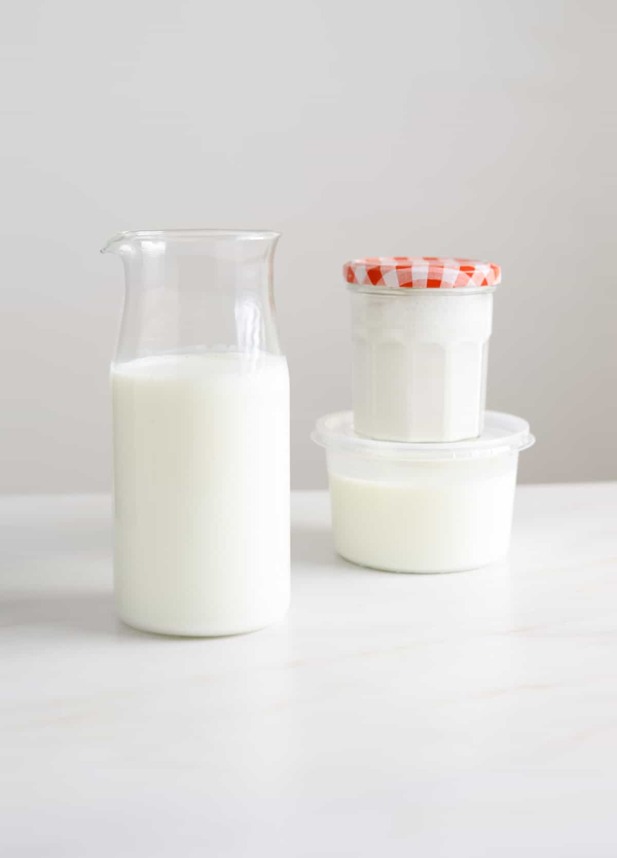 Three glass containers filled with buttermilk on a white marble background.