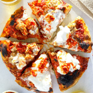 a pizza cut into six pieces surrounded by two chilled glasses of beer