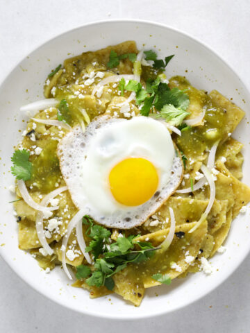 A white bowl filled with chilaquiles verdes topped with cilantro, onion and a fried egg.
