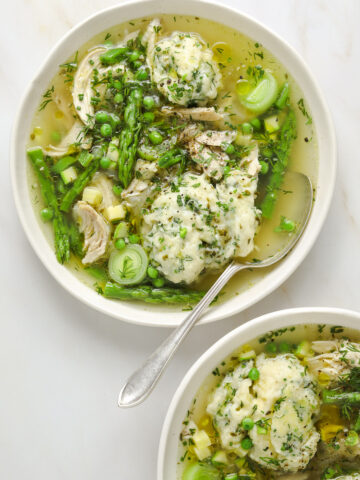 a white bowl filled with chicken soup and herb dumplings, asparagus, peas and leeks.