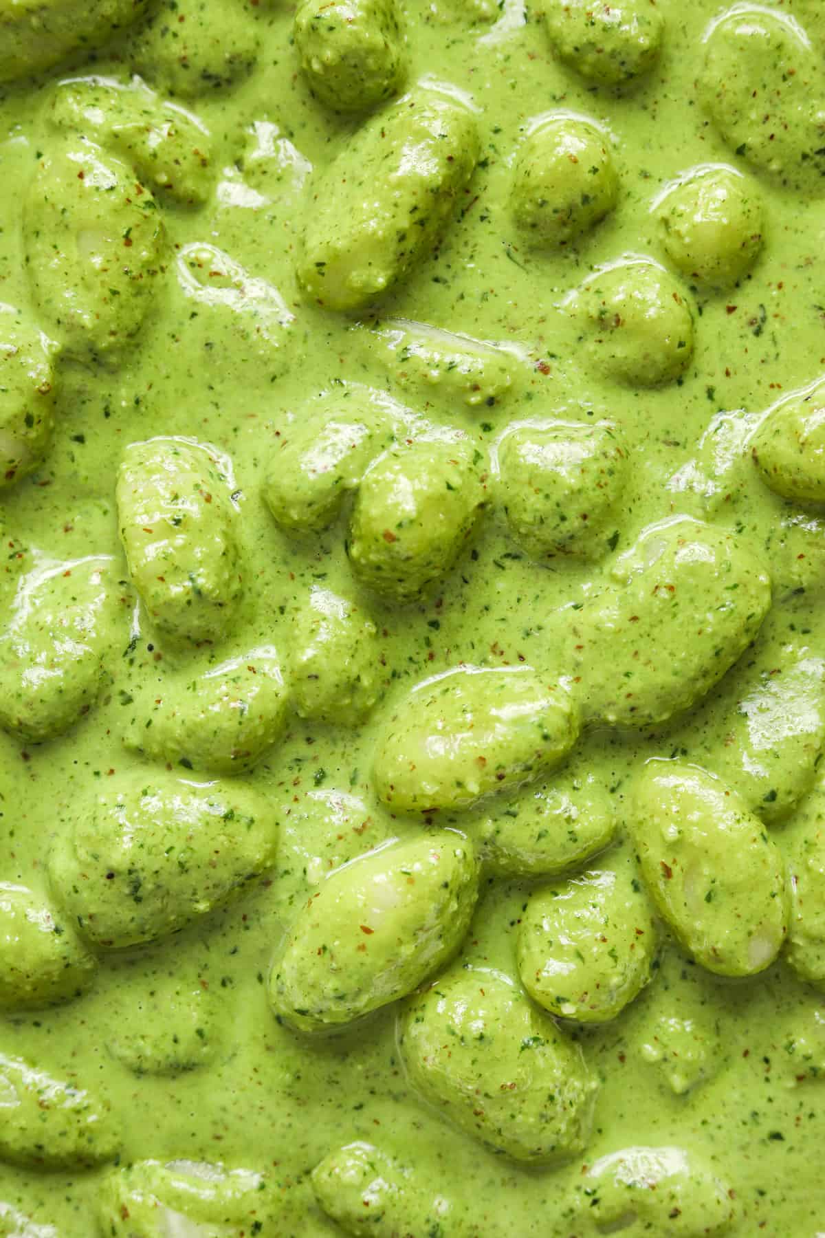A close up image of gnocchi with vibrant green pesto sauce.