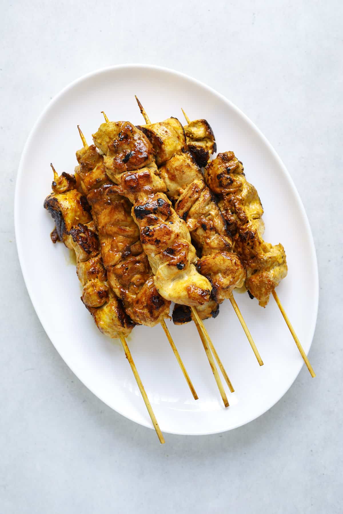 A white oval platter filled with 6 chicken skewers.