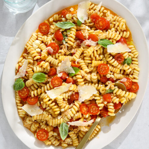 A large oval platter filled with pasta, cherry tomatoes, shaved parmesan cheese and fresh basil.