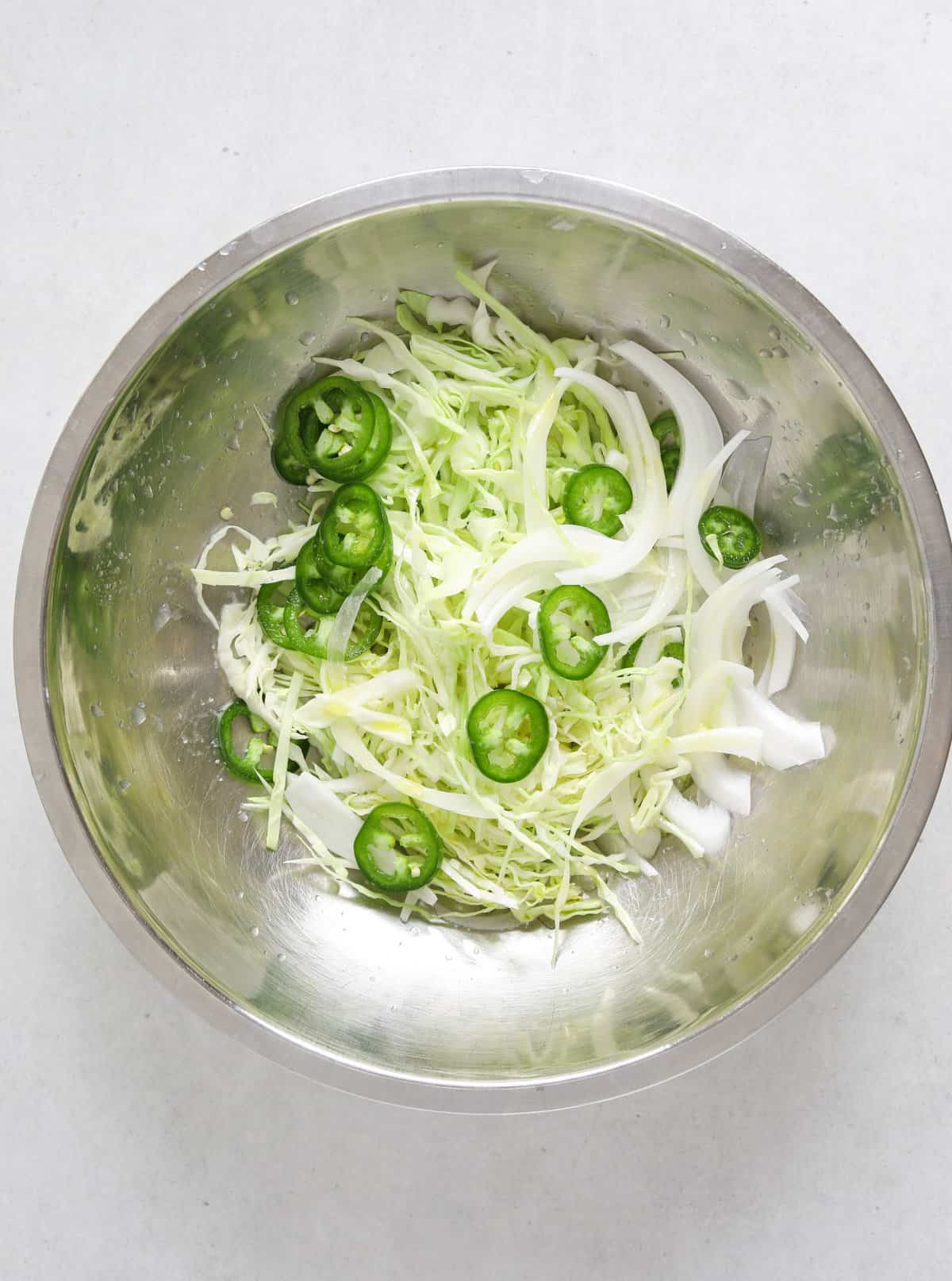 a stainless steel mixing bowl filled with shredded cabbage and sliced jalapeño.