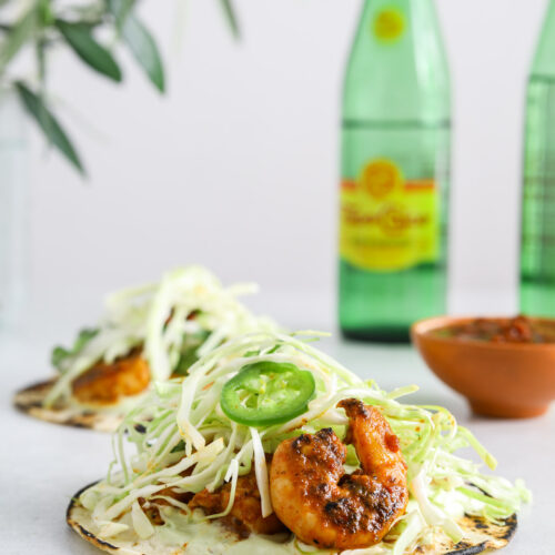 A close up image of a taco with shrimp and cabbage. Two green bottles of Topo Chico mineral water in the background.