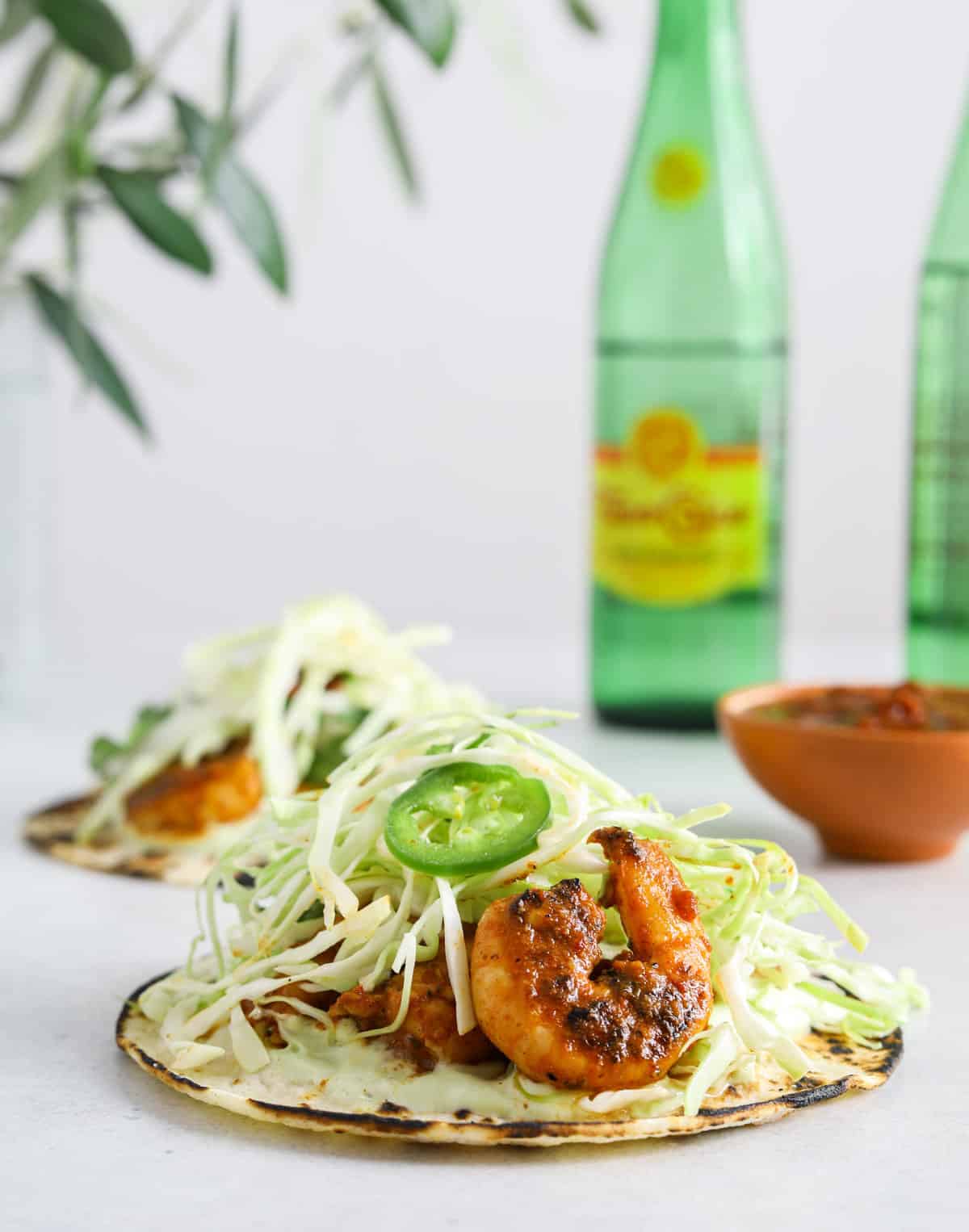 A close up image of a taco with shrimp and cabbage. Two green bottles of Topo Chico mineral water in the background.