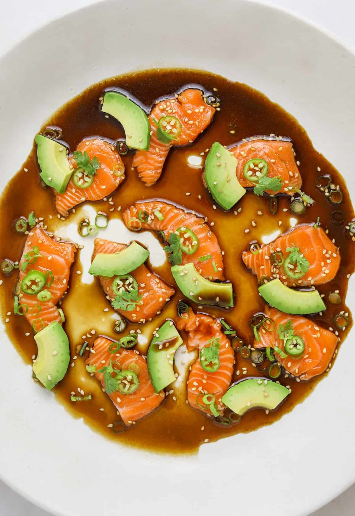 a round white platter with sliced salmon, avocado pieces, sesame seeds and cilantro.