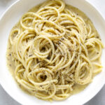 A white bowl filled with bucatini pasta and creamy black pepper sauce on a blue background.