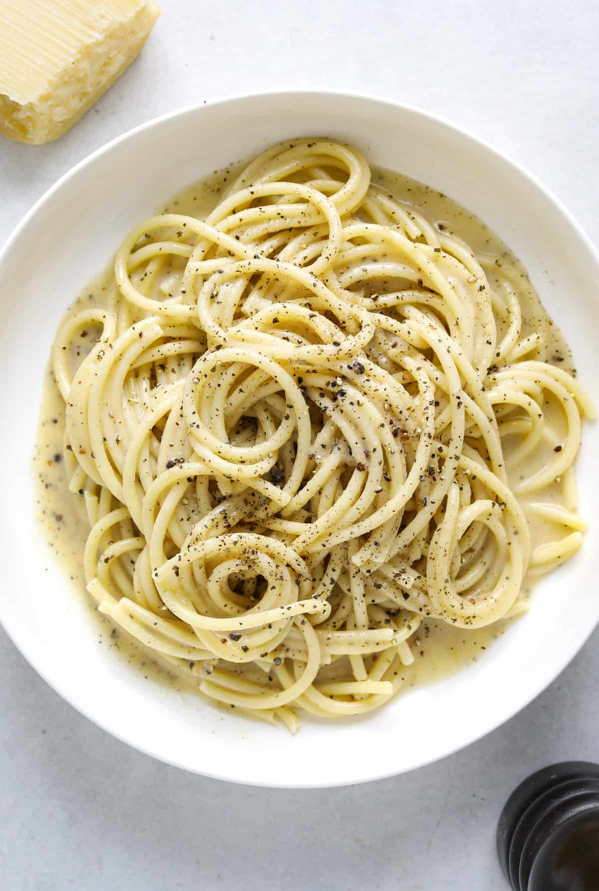 A white bowl filled with bucatini pasta and creamy black pepper sauce on a blue background.