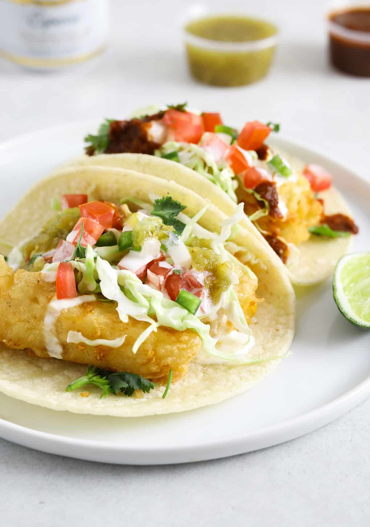 A close up image of a fried fish taco topped with cabbage slaw, diced tomatoes, and salsa.