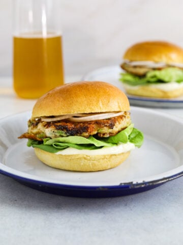 A chicken burger with lettuce, mayo and onion on a brioche bun with a beer in the background.