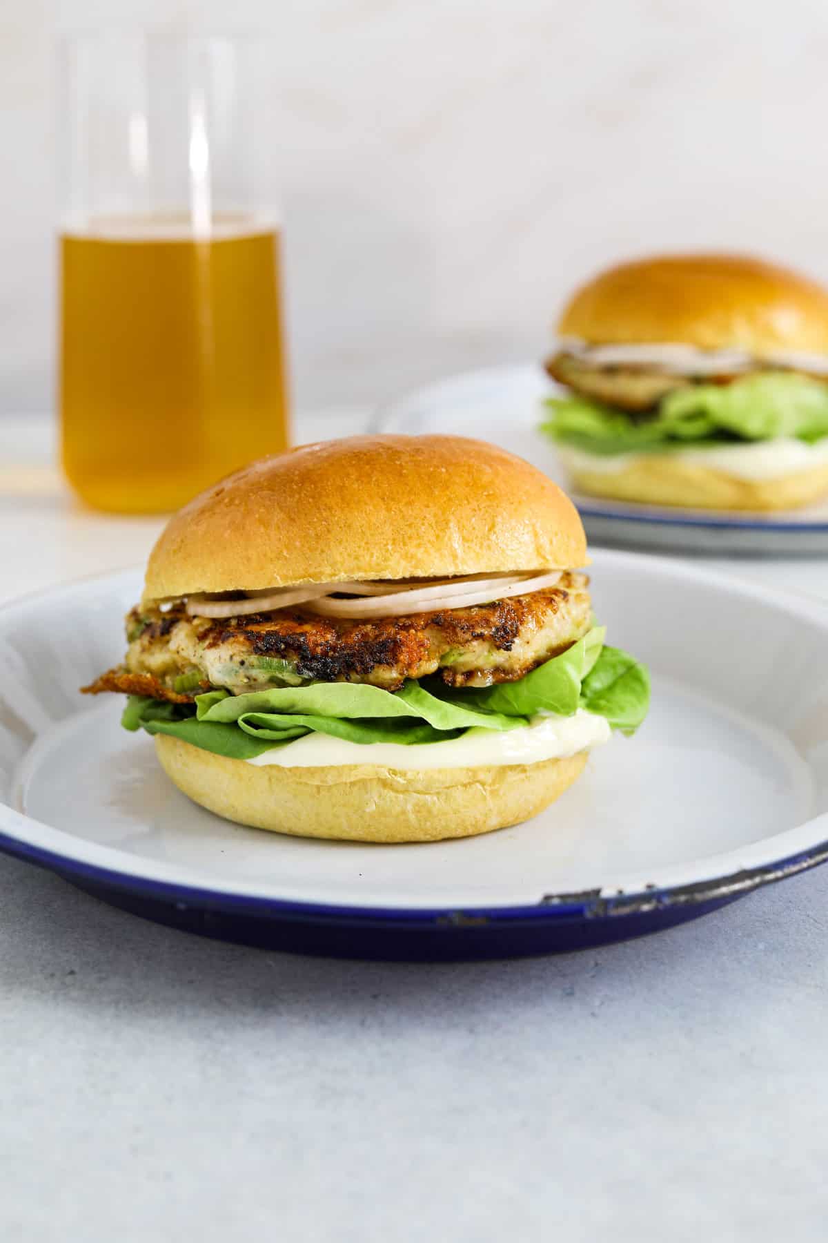 A chicken burger with lettuce, mayo and onion on a brioche bun with a beer in the background.