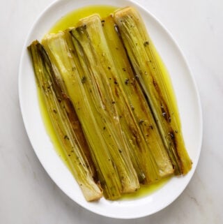 A white oval platter with roasted leeks and olive oil.