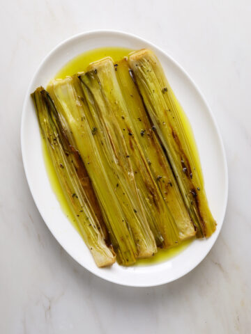 A white oval platter with roasted leeks and olive oil.