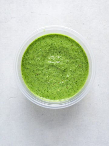 A plastic deli cup filled with vibrant green herbs sauce.