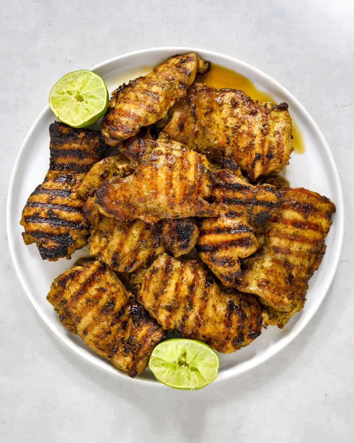 A white plate filled with bright and glossy grilled chicken thighs with black and brown grill marks.