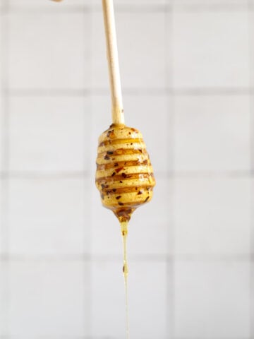 A honey dipper coated and dripping with honey and crushed red pepper flakes on a white background.