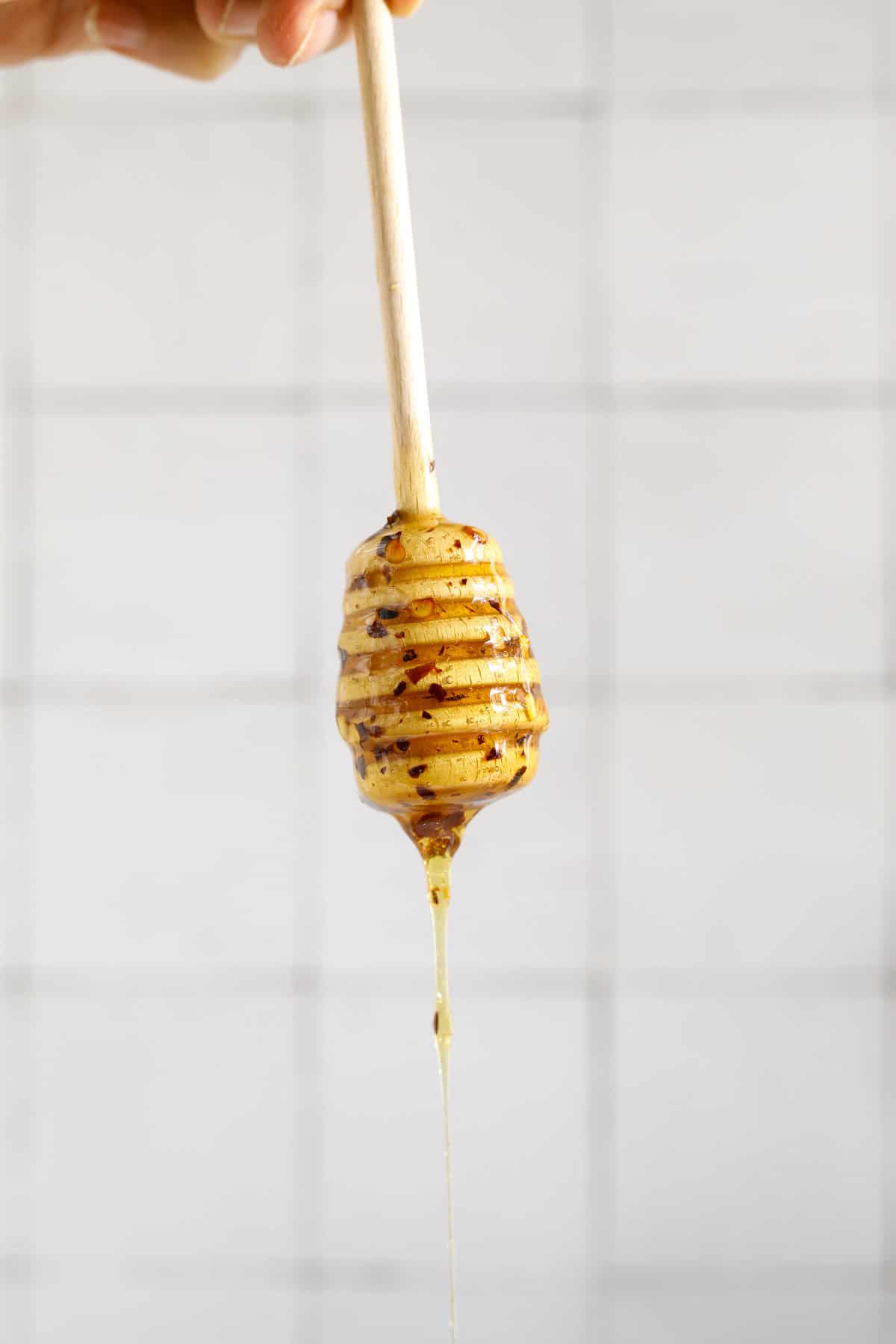 A honey dipper coated and dripping with honey and crushed red pepper flakes on a white background.
