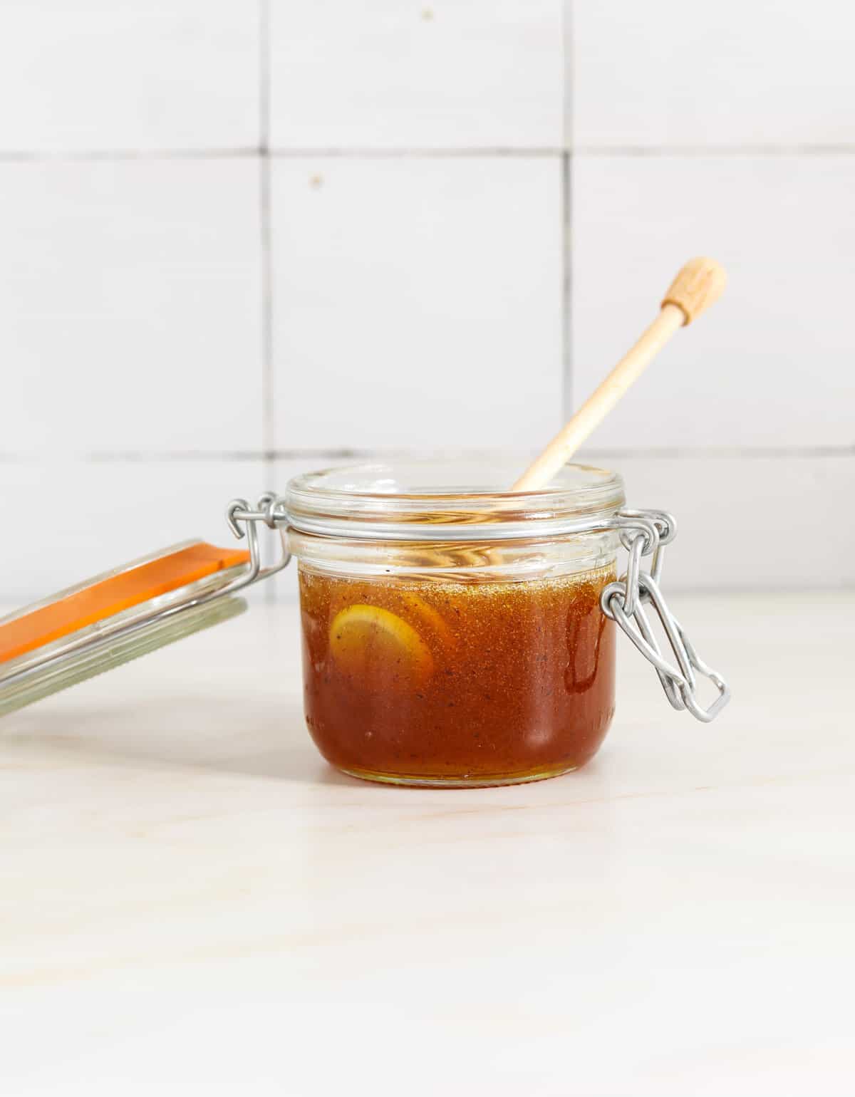 A small glass jar filled with honey and a wooden honey dipper hanging out the side.