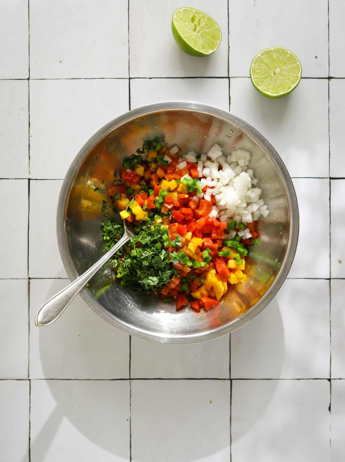 A small stainless steel mixing bowl filled with diced pico de gallo ingredients and a silver spoon for mixing.