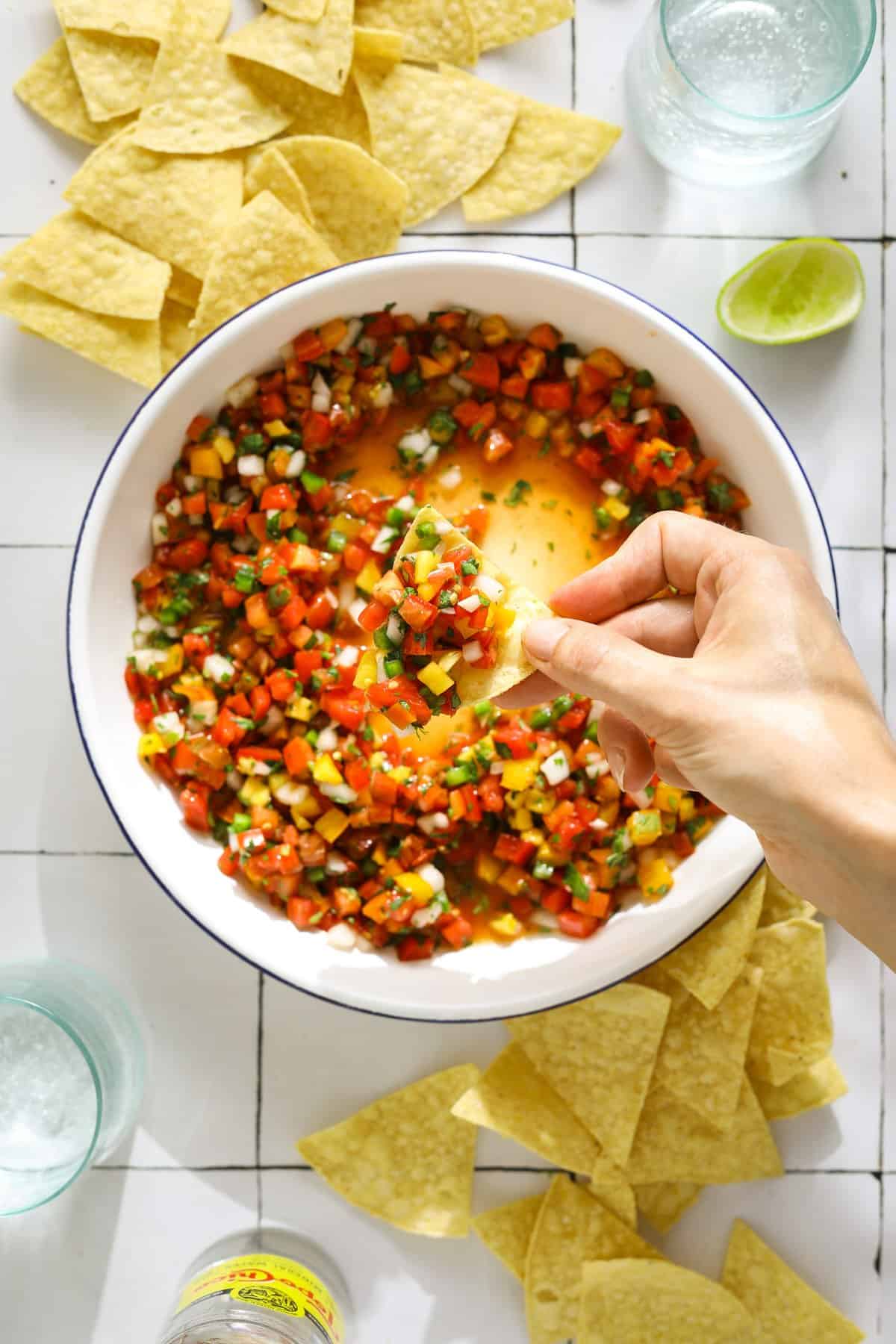 A white and blue enamel bowl filled with salsa and a hand holding a chip filled with salsa.