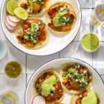 Two white and blue enamel plates filled with chicken tacos topped with salsa on a tile background.
