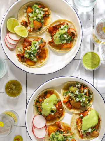 Two white and blue enamel plates filled with chicken tacos topped with salsa on a tile background.