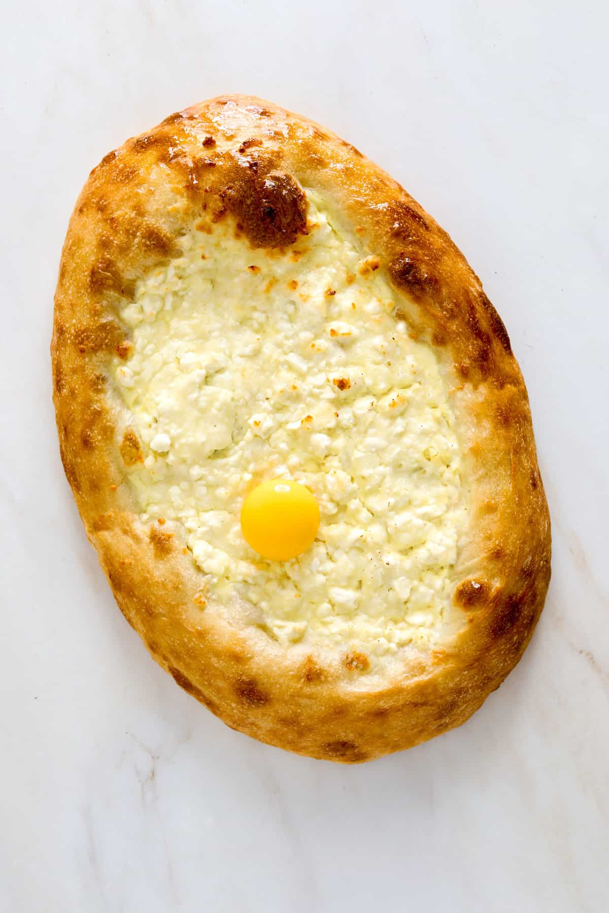 An oval pizza with golden brown crust filled with melty, white cheese and topped with an egg yolk.