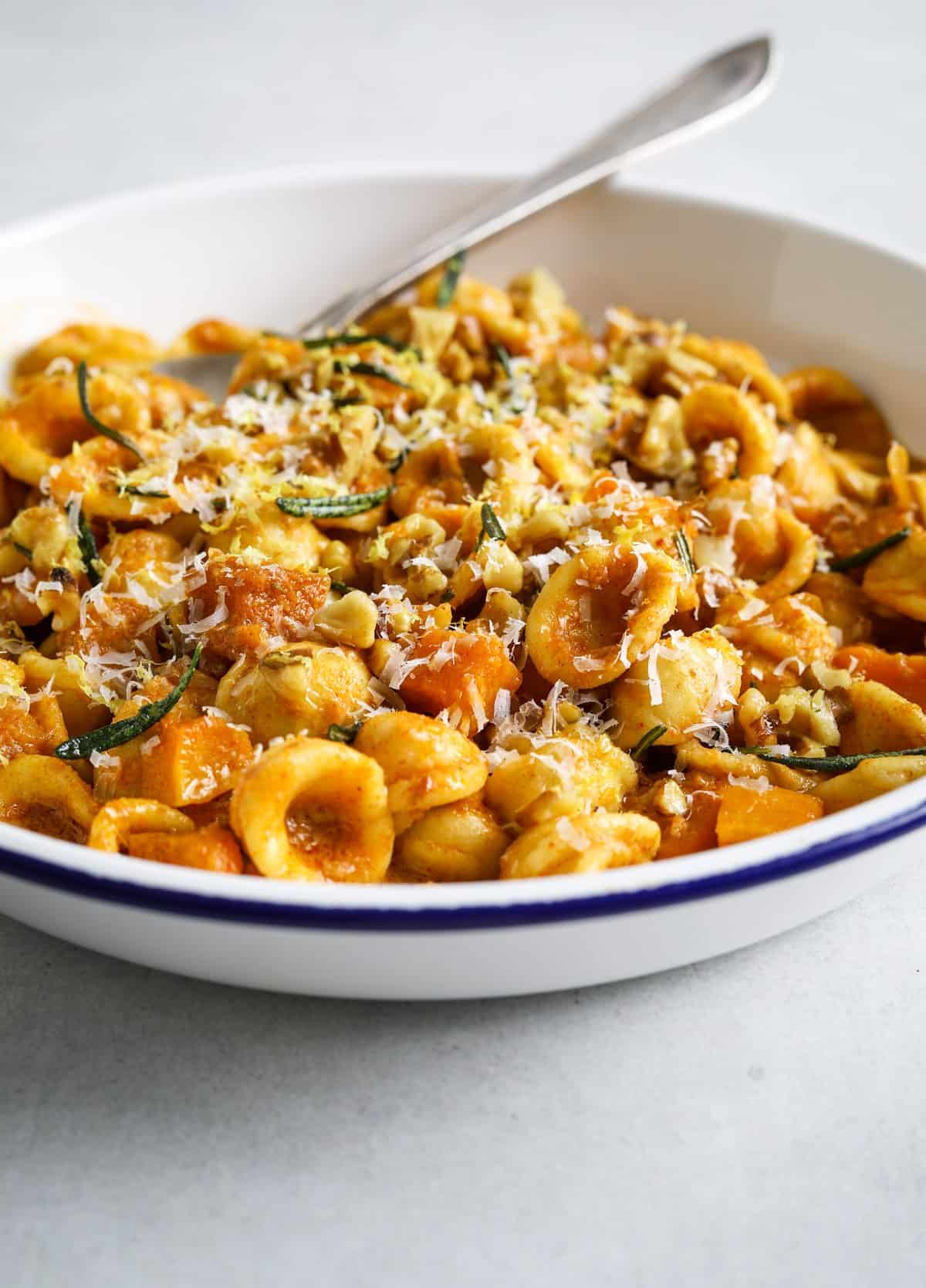 A close of of a bowl of orecchiette pasta with squash, rosemary and walnuts.