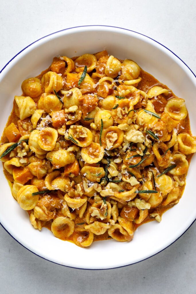 A white bowl with a blue rim filled with orecchiette pasta, cubed squash, rosemary and walnuts.