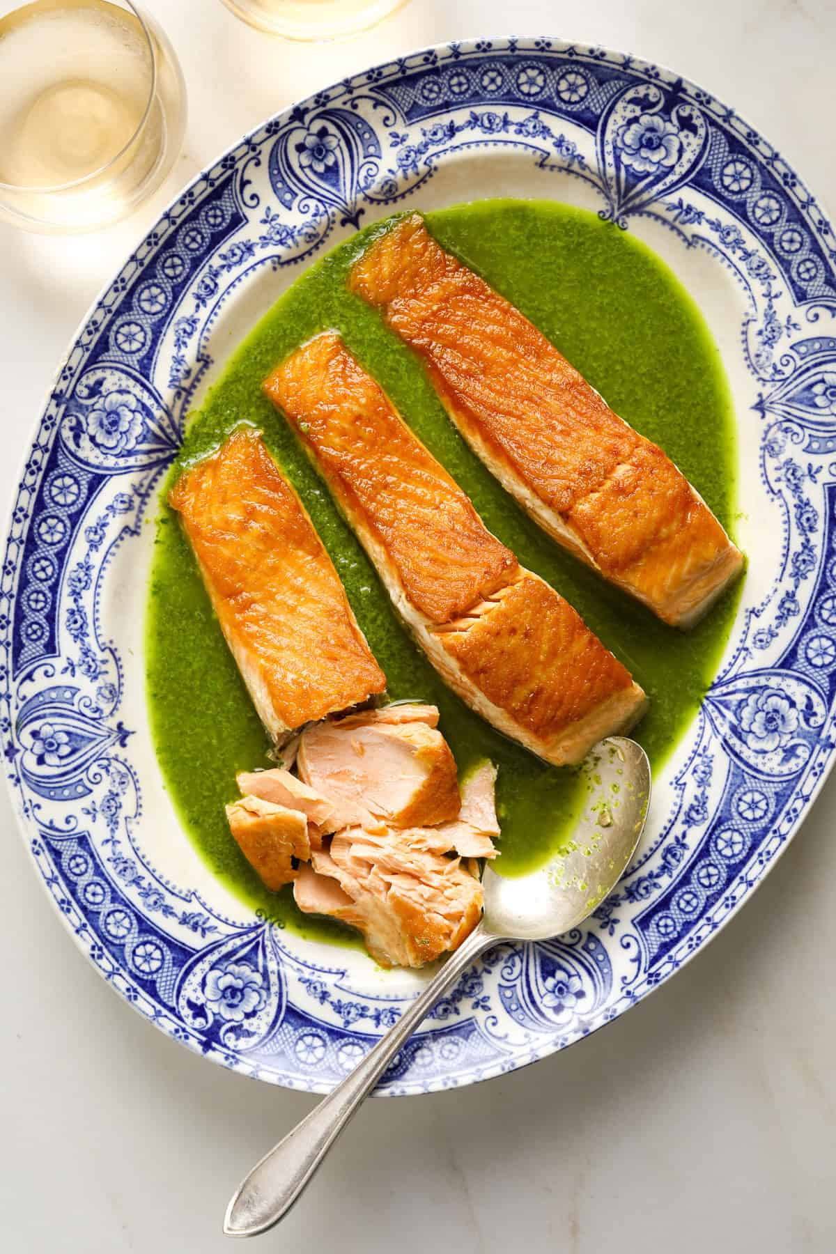 A blue and white platter with three salmon filets and a green herb sauce.