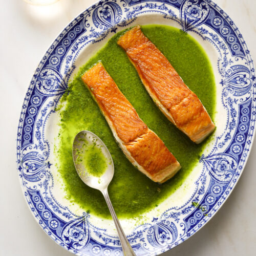 A blue and white antique platter with bright green sauce and two salmon filets.