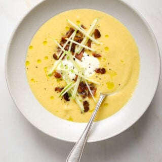 A bowl of carrot and parsnip soup with a soon dipping in from the side.