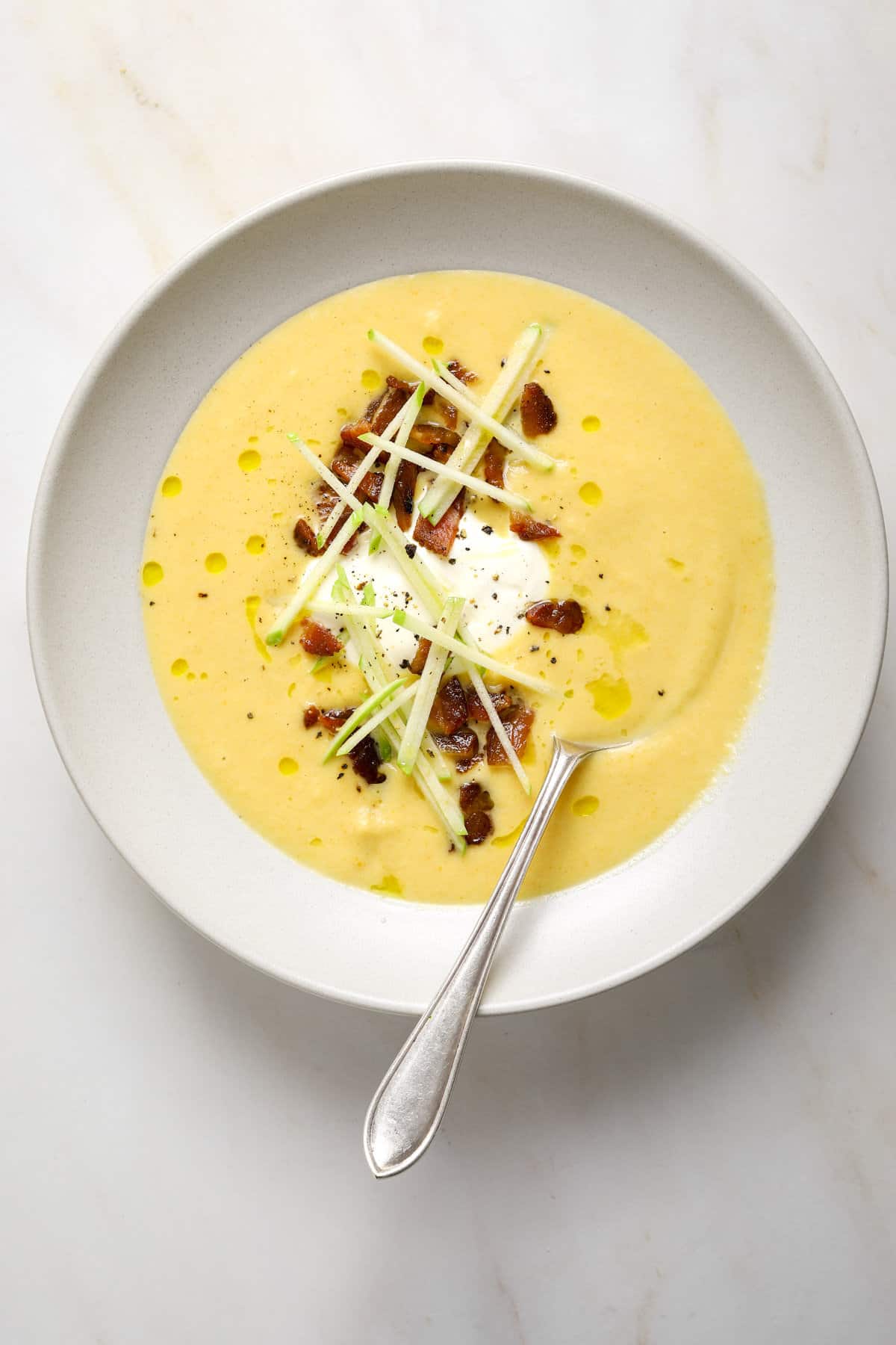 A bowl of carrot and parsnip soup with a soon dipping in from the side.