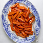 A blue and white antique platter filled with glossy roasted carrots with maple glaze.